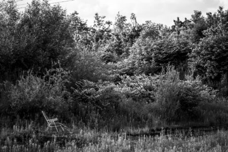 Copyright: Agnieszka Budzyńska Puste krzesło plażowe rozłożone na tle krzaków.